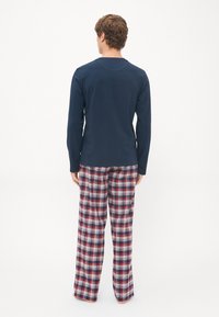 Camisa de manga larga en color navy combinada con pantalones de pijama de cuadros en rojo, azul y blanco. Tela de algodón, corte relajado y diseño de pierna ancha.