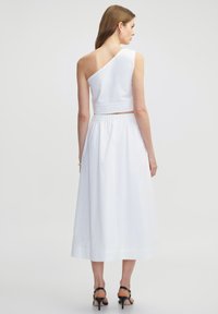 Bílý dvoudílný šat s kombinací bavlny, zahrnující asymetrickou crop top bez ramínka a polodlouhou, lehkou sukni s elastickým pasem.