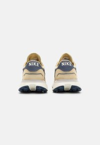 Nike sports shoes featuring a beige suede upper, navy accents, white logo at the heel, and textured rubber sole with a multi-directional tread.