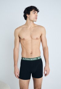 Fekete boxer alsónemű zöld derékrésszel, rajta "BJÖRN BORG" felirattal. Az anyag sima, testhezálló és rugalmas. A modell egy semleges háttér előtt áll.