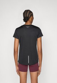 Fekete atlétikai póló rövid ujjakkal, kerek nyakkivágással és fényvisszaverő részlettel a hátoldalon, bordó rövidnadrággal párosítva. Simább textúra.