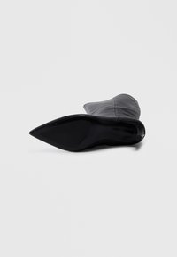 Black ankle boot with a pointed toe, smooth leather upper, and a sleek design. Features a thin heel and a solid black rubber sole.