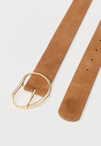 Ceinture en daim beige avec une grande boucle en métal doré lisse. Présente une surface plate et texturée avec plusieurs trous d'ajustement le long de la sangle.