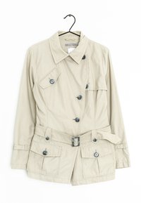 Cappotto corto beige con un design strutturato, dotato di vita regolabile con cintura, quattro tasche frontali e bottoni scuri, appeso a un gancio.