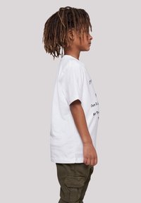 White t-shirt with short sleeves and black text. Paired with olive green cargo pants. Child with long, textured hair viewed from the side.