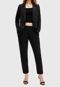 Musta räätälin bleiseri ja siihen sopivat slim-fit-housut, joissa on sileä kangas, lyhyt musta toppi ja avonaiset mustat korkokeng�ät.