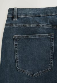 Dark blue denim jeans featuring a back pocket with a subtle stitched outline and a smooth texture, showcasing a classic cut and fit.
