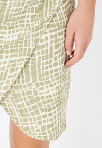 Falda asimétrica en verde claro y crema con un patrón de cuadrícula; textura suave, tela blanda y un detalle en el dobladillo.