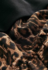 Țesătură neagră cu nervuri, stratificată peste o țesătură netedă de culoare maronie cu un model de leopard, având texturi moi și detalii plisate.