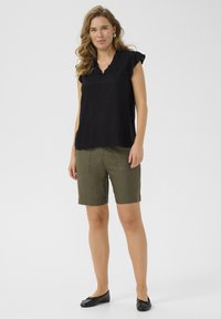 Black short-sleeve top with ruffled neckline, paired with olive green knee-length shorts. Flat black ballet shoes complete the outfit.