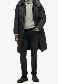 Czarna pikowana kurtka z kapturem, szary prążkowany sweter z golfem, czarne jeansy oraz czarne buty sznurowane. Elementy charakterystyczne to widoczne zamki błyskawiczne i przeszycia.