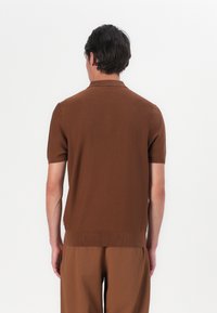 Polo castanho de manga curta com colarinho, textura de malha, bordas limpas e design ajustado. Combinado com calças castanhas a condizer.