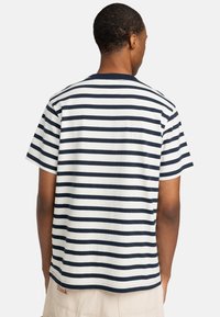 Camiseta a rayas con rayas horizontales alternadas en azul marino y blanco, cuello redondo, mangas cortas y una pequeña etiqueta bordada en el dobladillo.