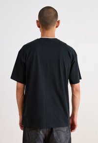 T-shirt en coton noir avec une coupe décontractée, des manches courtes et un col rond. Dos uni sans logos ou motifs visibles.