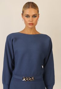 Granatowy sweter prążkowany z szerokim dekoltem, dopasowanym krojem, długimi rękawami i złotym łańcuchem jako akcentem w talii. Miękka tekstura.