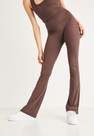 Brune flared leggings i strækstof med høj talje og glat tekstur. Parret med hvide sneakers for kontrast.