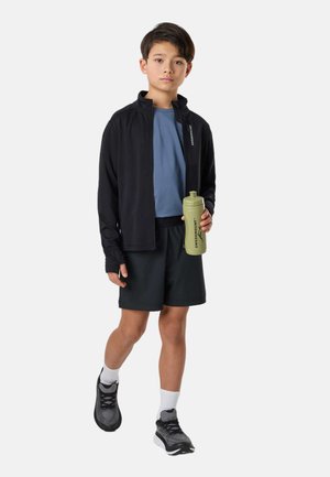 Dreng iført sort jakke, blå skjorte, sorte shorts og sneakers, holder en grøn vandflaske med "Swedemount" logo, går fremad.