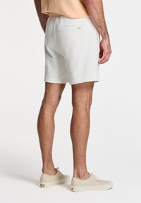 Hvide bomulds shorts med elastisk talje og en baglomme. Parret med beige snøre sneakers. Enkelt design, afslappet pasform.
