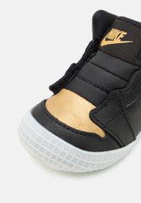 Scarpa da ginnastica nera e oro con tomaia in pelle testurizzata, linguetta in tessuto, collarino imbottito e suola in gomma bianca con motivo a griglia.