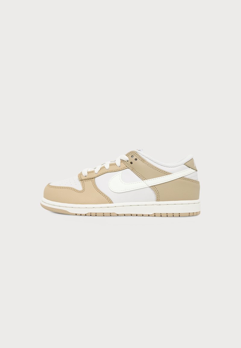 Nike sneaker χαμηλού παπουτσιού σε μπεζ και λευκό με λευκά κορδόνια και λευκό λογότυπο swoosh στο πλάι, εμφανίζεται σε απλό φόντο.