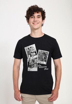 Sort bomulds T-shirt med et vintage-inspireret grafisk design, der indeholder tre sort-hvide billeder relateret til "The Sooty Show" samt tekstakcenter.