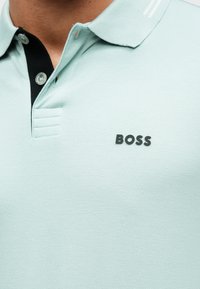 Világoskék poloing texturált anyagból, fekete gallérral és három gombbal. A mellrészen jól látható fekete "BOSS" logó.