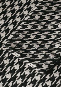 Schwarzes und weißes Hahnentritt-Muster auf einem Stoff mit glatter Textur, der eine umgeschlagene Kante hat, die das Design deutlich zeigt.