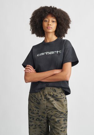 Čierne bavlnené tričko s logom Carhartt, krátke rukávy, v kombinácii s voľnými olivovo zelenými nohavicami s leopardím vzorom a elastickým pásom.