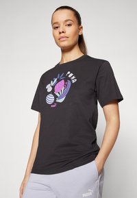 Tricou din bumbac negru cu un grafic floral colorat și cuvântul "Puma", completat de pantaloni de trening gri deschis cu detalii ale logo-ului.