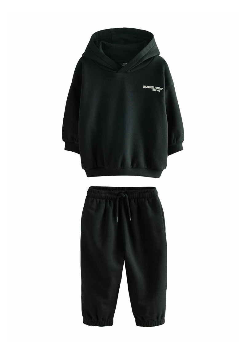 Čierna mikina s kapucňou a zodpovedajúci jogger set vyrobený z jemnej látky. Mikina má voľný strih a predný potlač, elastické manžety a pás.