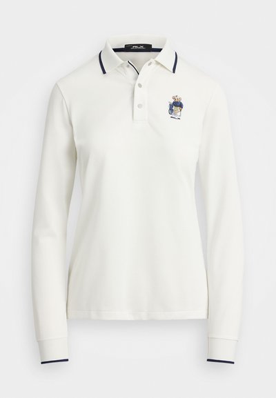 Ilgaaukštis baltas polo marškinėliai su raukšlėta apykakle ir tamsiai mėlynais akcentais, turintys siuvinėtą logotipą kairėje krūtinės pusėje. Lygus medvilnės audinys.