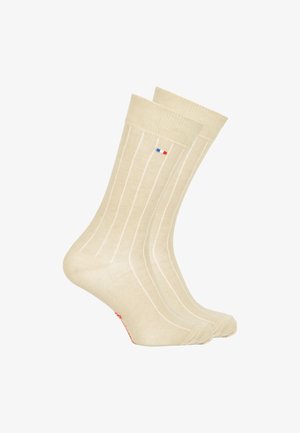 Chaussettes de couleur crème avec de légères rayures verticales, fabriquées en tissu doux, dotées d'un petit logo bleu et rouge près du bandeau supérieur et d'un accent rouge.