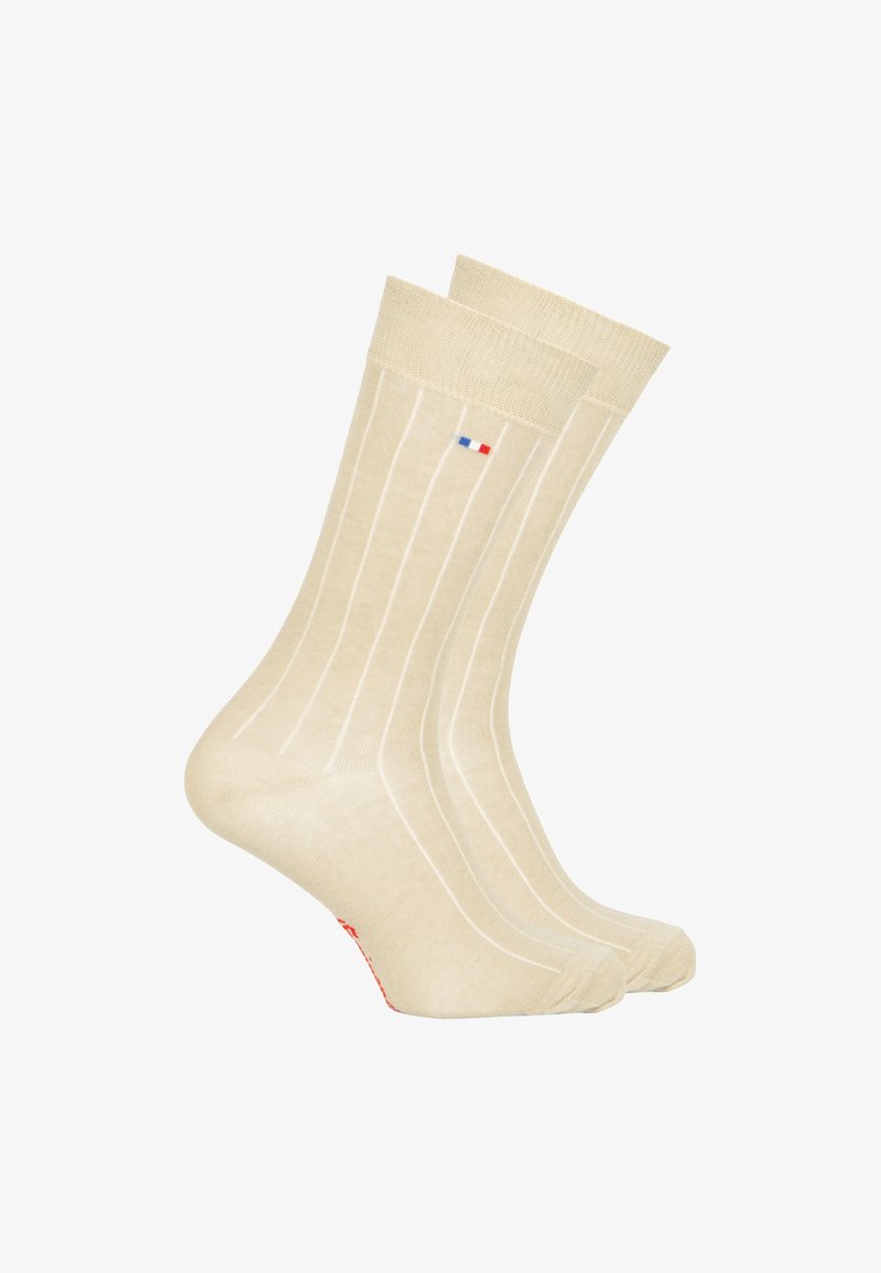 Chaussettes de couleur crème avec de légères rayures verticales, fabriquées en tissu doux, dotées d'un petit logo bleu et rouge près du bandeau supérieur et d'un accent rouge.