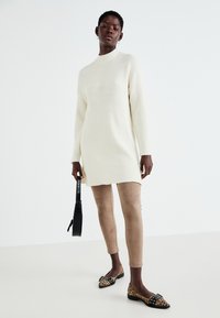 Robe pull côtelée crème à manches longues, associée à un pantalon slim beige clair et des ballerines à imprimé léopard avec des accents noirs.