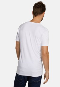 Witte T-shirt met korte mouwen en ronde hals, met een gladde textuur en een slim-fit ontwerp, gezien vanuit de achterkant. Draagt een blauwe spijkerbroek.