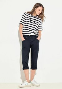 Randig huvtröja med dragsko i marinblått och vitt, kombinerad med marinblå cropped byxor med knappar och upprullade ärmar, kompletterat med vita sneakers.