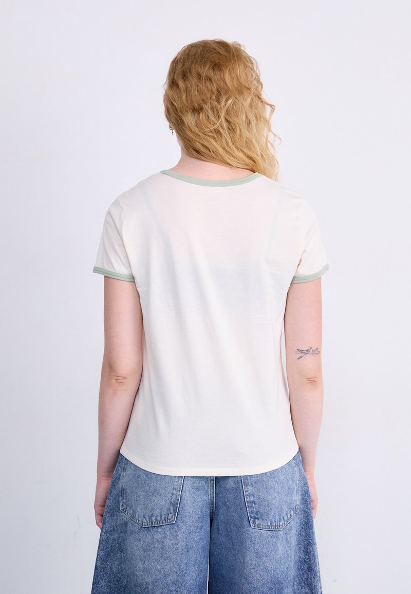 T-shirt a maniche corte color crema con bordi verde chiaro; tessuto morbido, colletto girocollo classico, orlo leggermente curvo e vestibilità comoda.