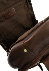 Brun læder rygsæk med en tekstureret overflade, der har en bronzefarvet lynlås, indvendig lomme og et mærket læderpatch indeni.