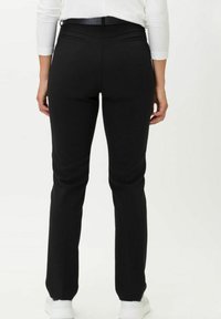 Pantaloni neri aderenti realizzati in un tessuto liscio, con due tasche posteriori e una vestibilità dritta; abbinati a calzature bianche.