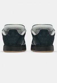 Black suede low-top sneakers with white lining, featuring a rubber sole and three white stripes on each side, emphasizing a textured design.