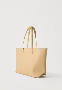Τσάντα tote από μπεζ δερματίνη με υφή, με δύο λεπτές λαβές και μπροστινή τσέπη, εμφανιζόμενη σε απλό λευκό φόντο.