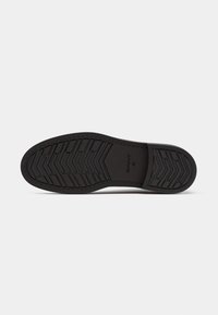 Suela de zapato de goma negra con patrón de pisada, con una superficie texturizada y una puntera redondeada. Marca estampada visible cerca del talón.