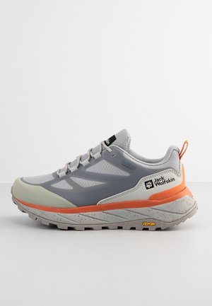 Zapato deportivo gris con parte superior de malla, detalles en naranja y suela de goma color marrón claro. Cuenta con logo grabado, puntera reforzada y banda de rodadura texturizada.