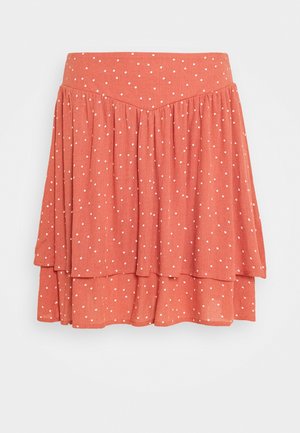 Jupe évasée en tissu corail avec des pois blancs. Elle présente une taille ajustée et des volants superposés pour ajouter de la texture et du mouvement.