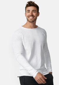 Camiseta blanca de manga larga con cuello redondo, hecha de tejido ligero. Presenta mangas ajustadas y un corte casual.