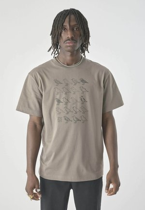 Tan cotton t-shirt with short sleeves featuring black graphic illustrations of various bird shapes on the front. Standard fit.