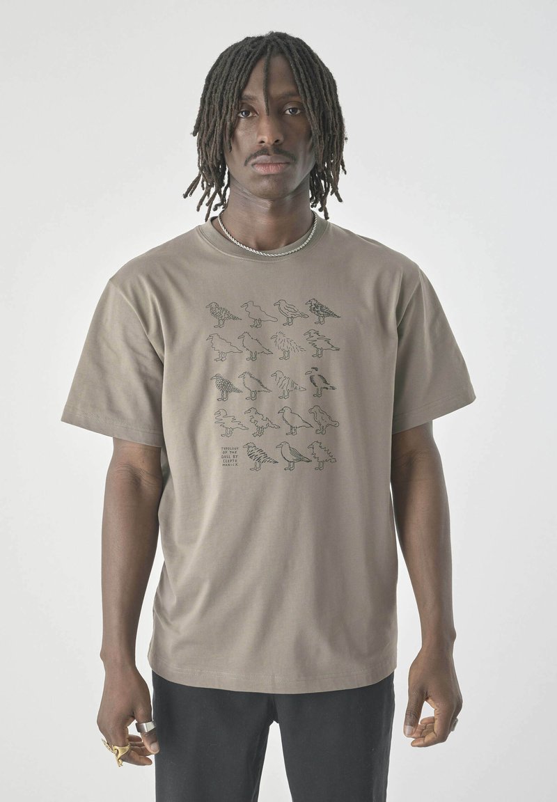 Tan cotton t-shirt with short sleeves featuring black graphic illustrations of various bird shapes on the front. Standard fit.
