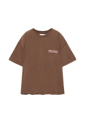 Hnedé extra veľké tričko s krátkymi rukávmi a ružovým nápisom "Gilda Season Small, Sweet, and Sassy" na ľavej strane hrudníka.