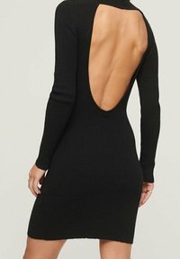 Svart stickad klänning med långa ärmar, en skärning i ryggen och en figurnära silhuett. Ribbad textur förstärker designens visuella tilltal.