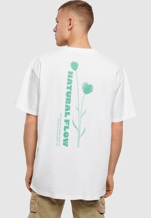 White cotton t-shirt featuring a green floral graphic design and text on the back, short sleeves, and a relaxed fit.